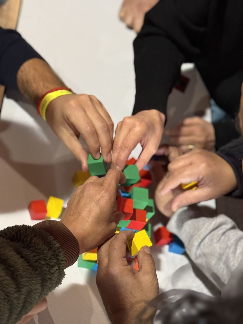Manos de un equipo construyendo juntos con bloques de colores durante un taller